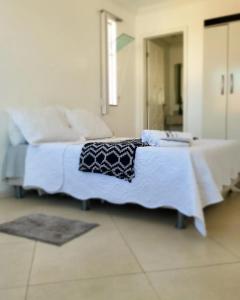 uma cama com lençóis brancos e um cobertor preto e branco em Pousada Pé na Areia Rio das Ostras em Rio das Ostras