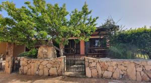 a house with a tree and a stone wall at Porto Pollo, Il borgo villetta 3 camere da letto in Porto Pollo