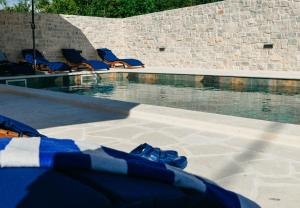 une piscine avec des chaises longues bleues à côté d'un mur de briques dans l'établissement Villa Marta, à Mala Čista