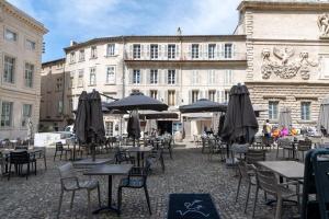 eine Terrasse mit Tischen und Sonnenschirmen vor einem Gebäude in der Unterkunft Un Cocon Au Cœur d'Avignon Logement in Avignon