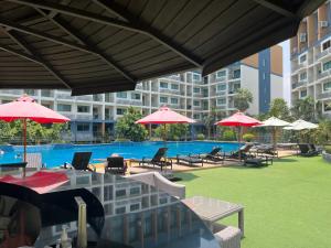 una piscina con mesas, sillas y sombrillas rojas en Jomtien Beach Laguna Resort 2 en Jomtien Beach