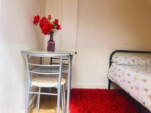 Garden Studio في لوتون: طاولة عليها إناء من الزهور الحمراء بجانب السرير