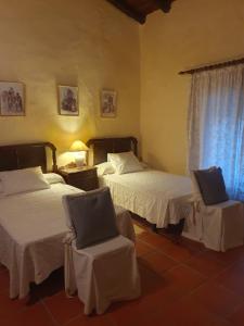1 dormitorio con 2 camas, silla y ventana en Hotel Rural El Vaqueril, en Navas del Madroño