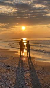 dos personas de pie en la playa viendo la puesta de sol en Apartament Jantarowe Zacisze Green, en Jantar