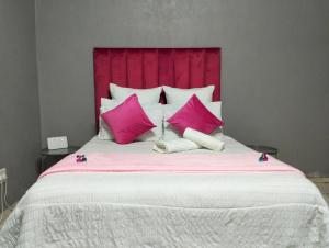 a large bed with pink pillows and a red headboard at O&S BnB in Centurion