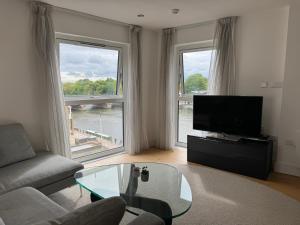 a living room with a couch and a tv and two windows at Entire Kingston Two bedroom Apartment Town centre & River view, 32 minutes to London Waterloo Station in London