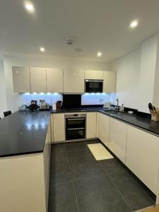 una cocina con armarios blancos y encimeras negras en Entire Kingston Two bedroom Apartment Town centre & River view, 32 minutes to London Waterloo Station en Londres