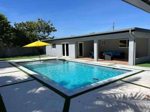 a swimming pool with a yellow umbrella next to a house at Renovated Villa resort pool, BBQ and Ping Pong Patio in Tamiami