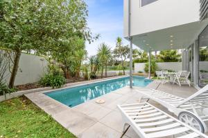 een zwembad met twee stoelen en een huis bij Sentinel Beach House - Auckland Holiday Retreat in Auckland