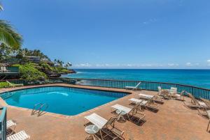 a swimming pool with chairs and the ocean in the background at Poipu Shores 207A in Koloa