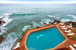 ein leerer Swimmingpool neben dem Meer mit Stühlen in der Unterkunft Poipu Shores 107A in Koloa