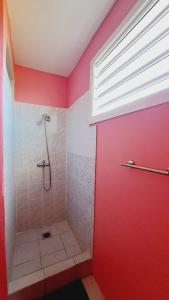 La salle de bains est pourvue d'une douche et d'un mur rouge. dans l'établissement La Baie de Coreil, à Bouillante