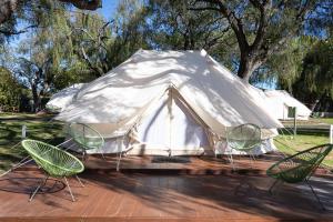 Busselton Villas and Glamping Village في بوسيلتون: خيمة بيضاء بأربعة كراسي وطاولة