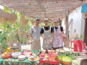 three people standing in front of a table with food at Happy Homestay SiemReap - Local Vibe in Phumĭ Puŏk Chăs