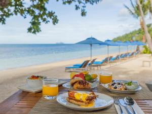 a table with breakfast food and orange juice on the beach at Explorar Koh Phangan - Adults Only Resort and Spa in Haad Rin