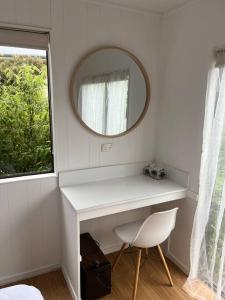 a white desk with a mirror and a chair at Beachside Gem - Cosy Chalet in Parapara 