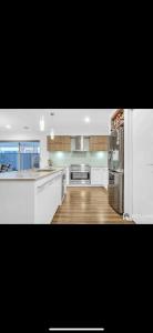 a large kitchen with white cabinets and a refrigerator at Home away from Home 22 mins from Airport and CBD in Truganina