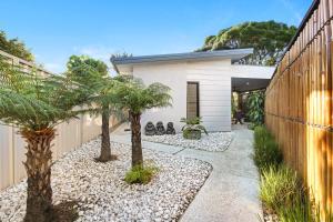 un patio trasero con palmeras y una casa blanca en Elvis on Brodie - luxury boutique accommodation en Coffs Harbour