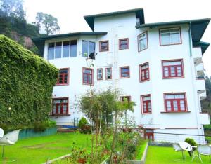een groot wit gebouw met rode ramen en een tuin bij New Ashley Resorts (PVT) LTD in Nuwara Eliya