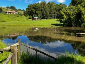 a pond with a fence and a house in the background at Incwala Lodge in Waterval Boven