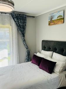 um quarto com uma cama com almofadas roxas e uma janela em Lakhe Lethu Apartment: Green Valley Estate em Nelspruit