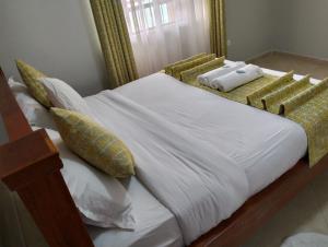 uma cama grande com lençóis brancos e almofadas amarelas em JNJ luxury homes em Naivasha