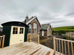 a house with a green and white door on a deck at Shepherds Hut at Maes Uldale in Uldale