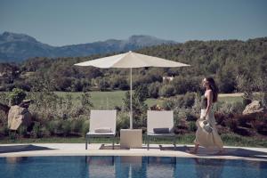 a woman walking by a swimming pool with an umbrella at Es Figueral Nou Hotel Rural & Spa - Adults Only - Over 12 in Montuiri