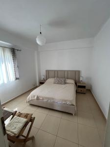 a white bedroom with a bed and a chair at Gkiko’s Guest House in Qeparo