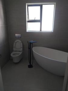 a bathroom with a tub and a toilet with a window at Beautiful No Fuss Serene 4-Bed House in Bulawayo in Bulawayo