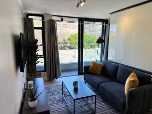 sala de estar con sofá azul y ventana grande en The Westwood Deluxe Studio, en Ciudad del Cabo