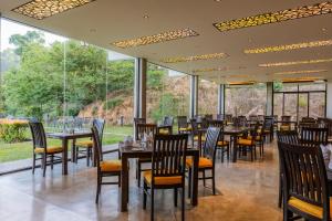 uma sala de jantar com mesas, cadeiras e janelas em Simpson's Forest Hotel em Kandy