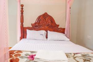 a bed with a wooden headboard and two towels on it at KaribuGuestHouse in Fort Portal