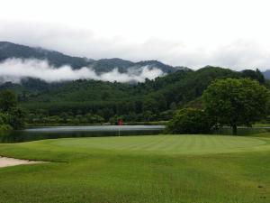 a golf course with a lake and mountains in the background at Katathong Golf Resort & Spa in Phangnga