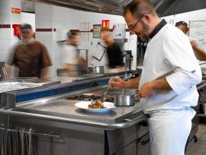 een chef-kok die een bord met eten bereidt in een keuken bij Mercure Mont Saint Michel in Le Mont Saint Michel