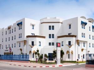 un bâtiment blanc avec une clôture bleue devant lui dans l'établissement Ibis El Jadida, à El Jadida