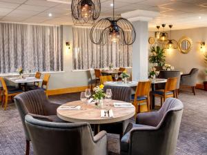 uma sala de jantar com mesas, cadeiras e lustres em The Harlow Hotel By AccorHotels em Harlow