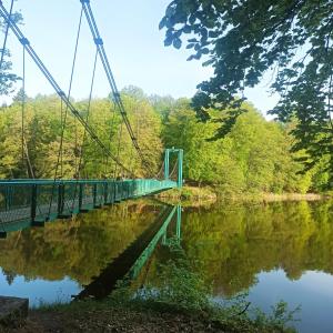 eine grüne Hängebrücke über einen Fluss mit Bäumen in der Unterkunft Pojezierze wałeckie kusi atrakcjami in Wałcz