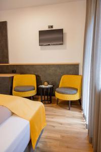 a hotel room with two beds and yellow chairs at Hotel Christin in Ora/Auer