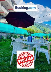 a white table with an umbrella on the grass at Hotel Hamta View Manali !! Top Rated & Most Awarded Property in Manali !! in Manāli