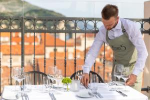 un hombre en un delantal poniendo una mesa con gafas en Boutique Hotel Stari Grad, en Dubrovnik
