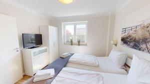 ein weißes Schlafzimmer mit einem Bett und einem Fernseher in der Unterkunft 54° Nord Wohnung 3 in Grömitz
