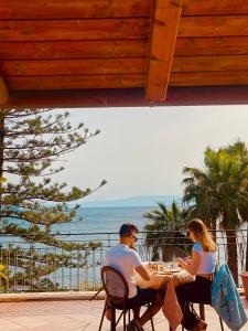 un hombre y una mujer sentados en una mesa mirando al océano en Hotel Baia Delle Sirene en Taormina
