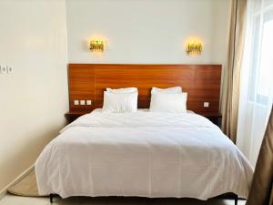 - une chambre avec un grand lit blanc et une tête de lit en bois dans l'établissement Medina Baye Résidence Boutique Hôtel, à Kaolack