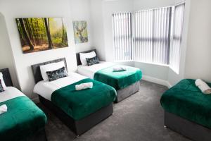 a room with three beds with green sheets and a window at 4 Bedrooms Spacious House With 2 Bathrooms Free Parking - sleeps up to 10 guests in Liverpool
