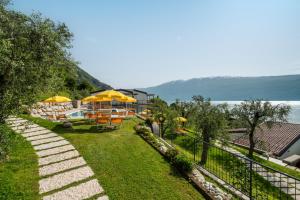 un jardín con mesas, sombrillas amarillas y agua en Residence Dany appartamenti con cucina vista lago piscina e parcheggio, en Gargnano