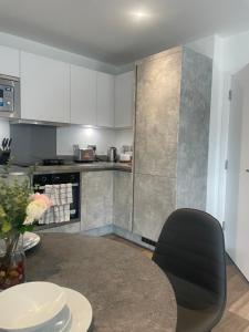 a kitchen with white cabinets and a table with a black chair at Brand New Stunning 2-Bed Apartment in Dagenham in Dagenham +2 photos