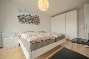 a white bedroom with a bed and a chair at Galerie Obersee 4C in Arosa