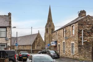 an old stone church with a tower and cars parked at Stylish Three Bed House Burnley in Burnley