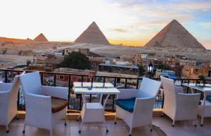 una mesa y sillas en un balcón con pirámides en el fondo en Royal Golden Pyramids Inn en El Cairo